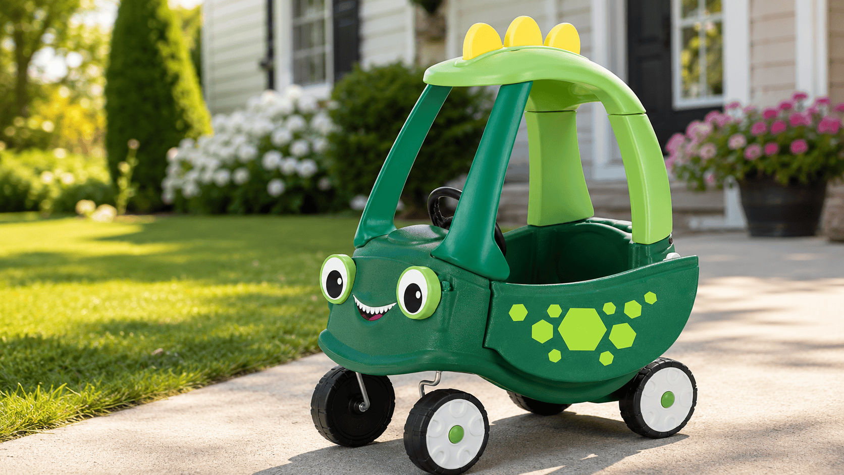 Little Tikes Cozy Coupe Dinosaur toy car on a sunny driveway beside a lawn and flowers outside a family home