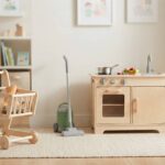 best pretend play toys for toddlers with a generic shopping cart, toy vacuum, and play kitchen in a bright playroom